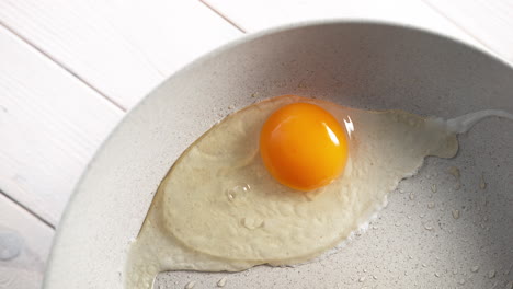 cracking eggshell and cooking sunny side-up egg in a frying pan in slow motion, view from behind the chef, showing his hands