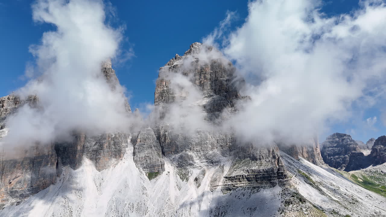 Dronebillede af de berømte Tre Cime di Lavaredo med tårnhøje klippespir, der rejser sig over alpemarier og vandrestier i Dolomitterne, et UNESCO verdensarvsområde.
