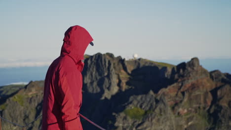 persona con chaqueta roja mirando las montañas con un observatorio a distancia