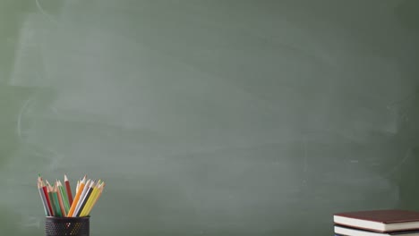 Video-of-books-and-cup-with-crayons-on-wooden-table-over-mathematical-formulas-on-blackboard