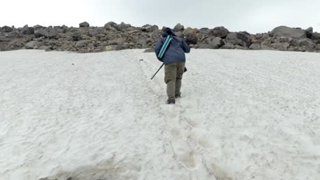 Guy-walking-up-snowy-slope-using-stick-for-balance,-back-view,-Mount-Asahi