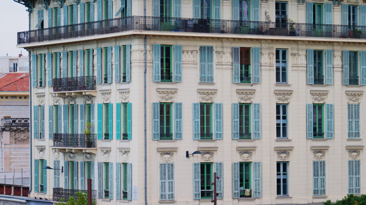 Multiple windows on the facade of a beige building with pastel turquoise shutters in Nice, France