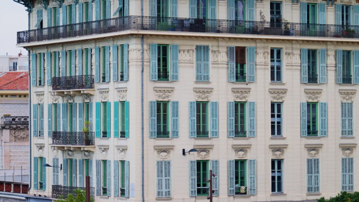 Molteplici finestre sulla facciata di un edificio beige con persiane color turchese pastello a Nizza, Francia
