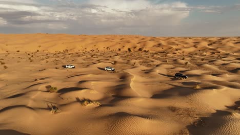 the drone is flying sideways following three cars driving through the sahara desert in tunisia aerial footage 4k