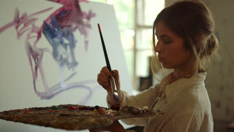 Young-woman-artist-drawing-in-studio.-Skilled-painter-using-palette-indoors.