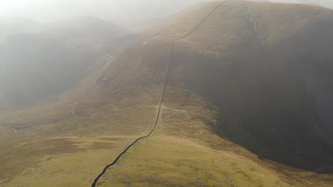 Mourne-wall-sprawls-along-foggy-heathland-grassy-plains-of-Slieve-Donard,-Ireland