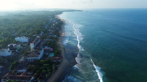 Aerial-drone-landscape-view-of-Hikkaduwa-coastline-with-morning-sunrise-ocean-sea-wave-beaches-with-resort-hotels-shops-Sri-Lanka-Asia-travel-tourism