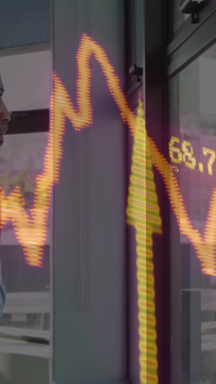 Vídeo vertical: Homem observando dados atualizando, fazendo com que um gráfico financeiro em vidro atinja o pico e depois caia.