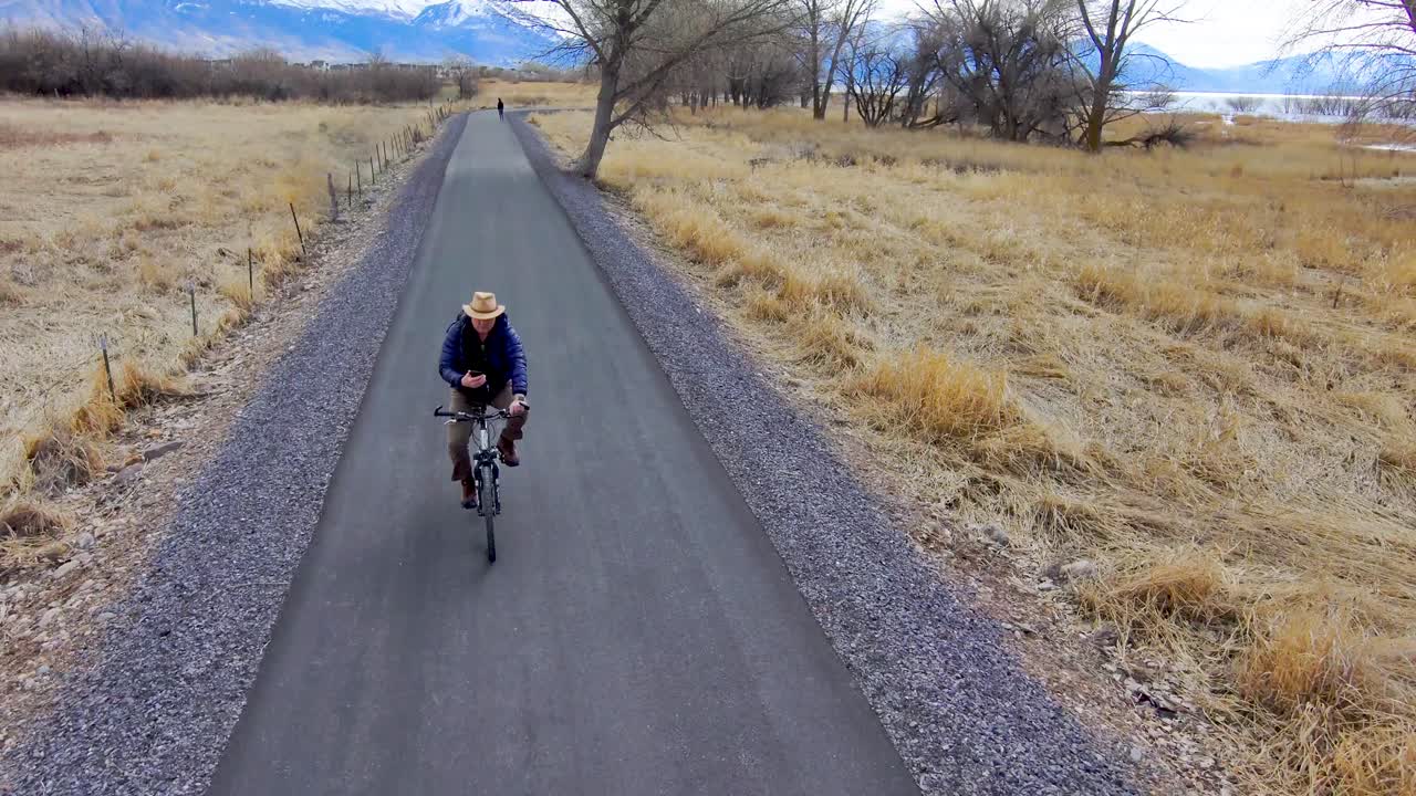 As a senior man bicyles along a nature trail, he checks his smartphone for messages or location - aerial view