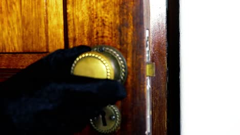 Brass-Door-knob-turns-and-man-with-black-glove-opening-wooden-door-slowly