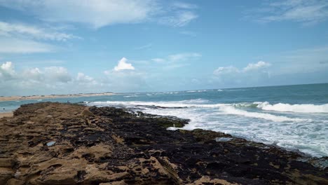 Tiro-Inclinado-De-Pequeñas-Olas-Que-Chocan-Contra-Rocas-Cubiertas-De-Algas-En-La-Popular-Playa-Tropical-De-Tibau-Do-Sul,-Donde-El-Océano-Atlántico-Se-Encuentra-Con-La-Laguna-De-Guaraíras-En-Río-Grande-Do-Norte,-Brasil