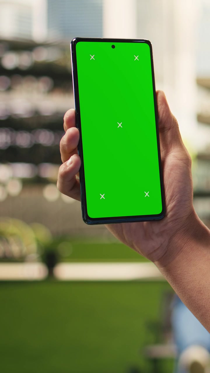 Mockup verticale di schermo verde per video su smartphone, tenuto da uno studente in camice blu.