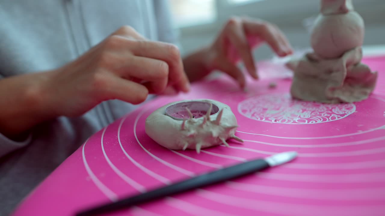 Primo piano di mani che modellano un portacandele in argilla su un tappetino rosa