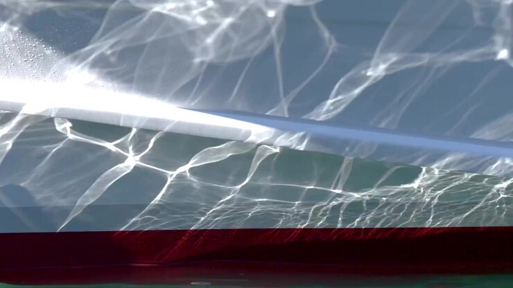Close-up shot of shimmering water reflections dancing across a white boat hull in sunlight.