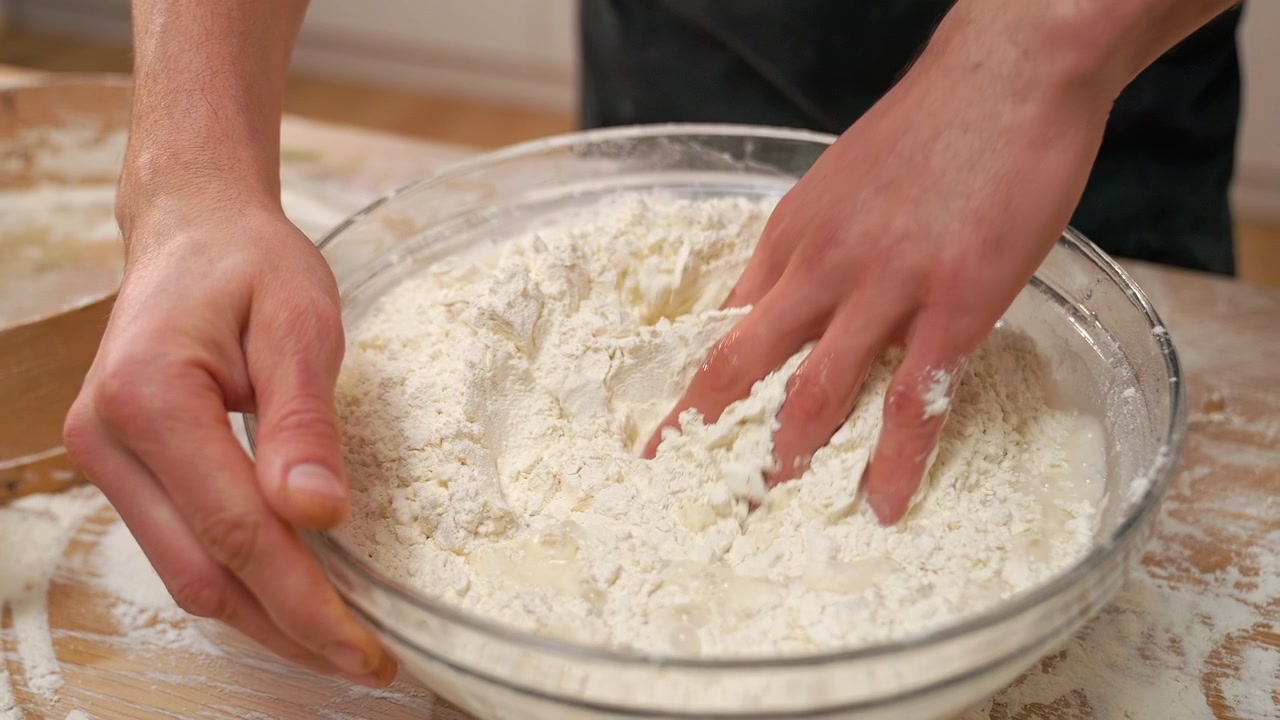 Primo piano di mani che mescolano farina e acqua per l'impasto
