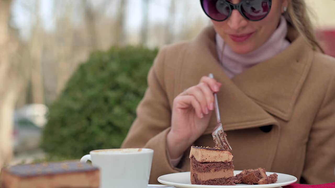 Woman in brown coat eating chocolate cake with coffee at a terrace