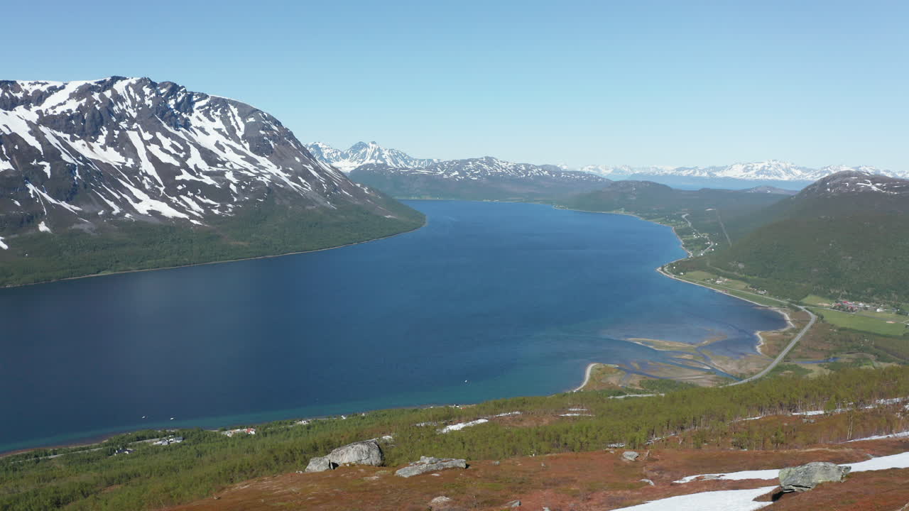 vista aérea de un hombre parado en una cornisa de montaña, mirando hacia abajo en un fiordo en el océano ártico, soleado, día de verano, en rotsund, troms, nordland, noruega - dolly, tiro de drone