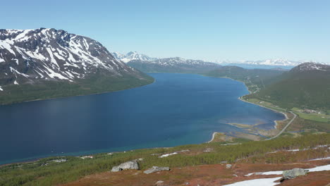 aerial view of a man standing on a mountain ledge, looking down on a fjord at the arctic ocean,, sunny, summer day, in rotsund, troms, nordland, norway - dolly, drone shot