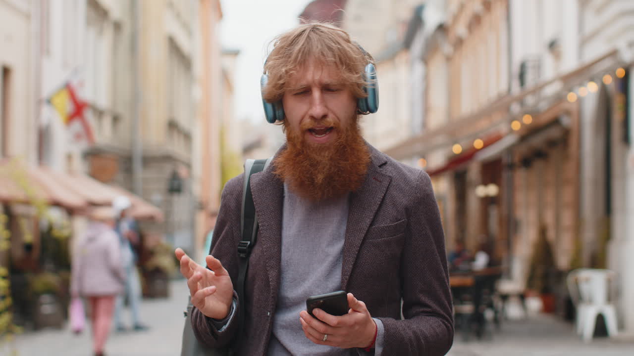 Glücklicher junger Mann mit drahtlosen Kopfhörern, der Musik im Smartphone hört und im Freien tanzt