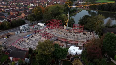 aerial view orbits crane building waterside care home construction framework in rural british village next to fishing lake