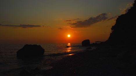 paisaje marino con playa rocosa bañada por el mar que refleja una hermosa puesta de sol con un cielo naranja nublado