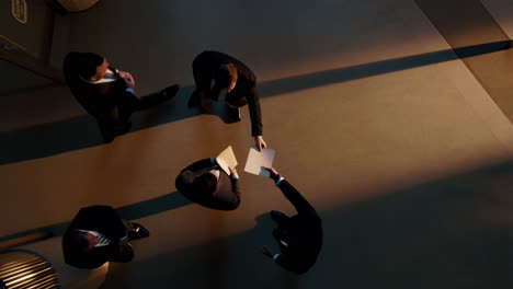 Overhead view of business professionals interacting, walking, and exchanging documents in a dimly lit office environment