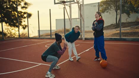 Primer-Plano-De-Una-Chica-Rubia-Con-Un-Peinado-Bob,-Un-Sombrero-Negro-Y-Un-Uniforme-Deportivo,-Junto-Con-Sus-Dos-Amigas,-Calentando-Antes-De-Jugar-Al-Baloncesto-Con-Una-Espada-Naranja-En-Una-Cancha-Roja-Al-Amanecer.