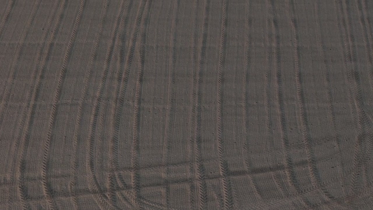 Cultivated farmland in the Po Valley near Cremona, Lombardy, Italy, revealing tractor tire tracks, tilled soil, agricultural field patterns and textured earth, top-down drone descent.