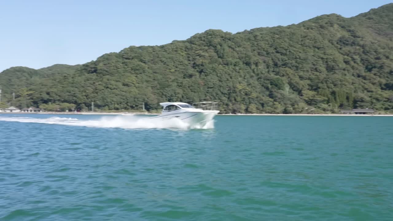 Ripresa in movimento di un motoscafo moderno bianco che sfreccia ad alta velocità attraverso acque azzurre lungo una costa boscosa.
