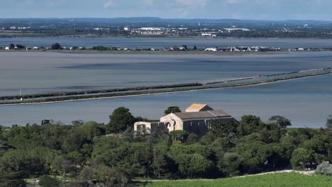 Maguelone-Cathedral-on-volcanic-island-over-the-lagoon-with-sandbar-roads,-Wide-reveal-aerial-shot