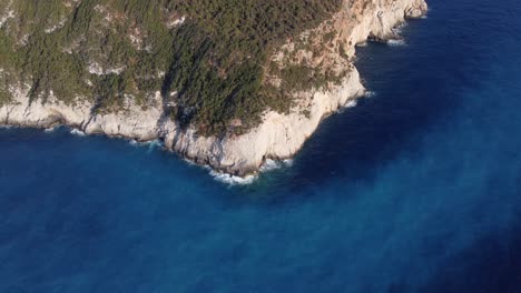 aerial: hill forest island cliff at sea shore with blue water at lefkada, greece: drone flying top down shot