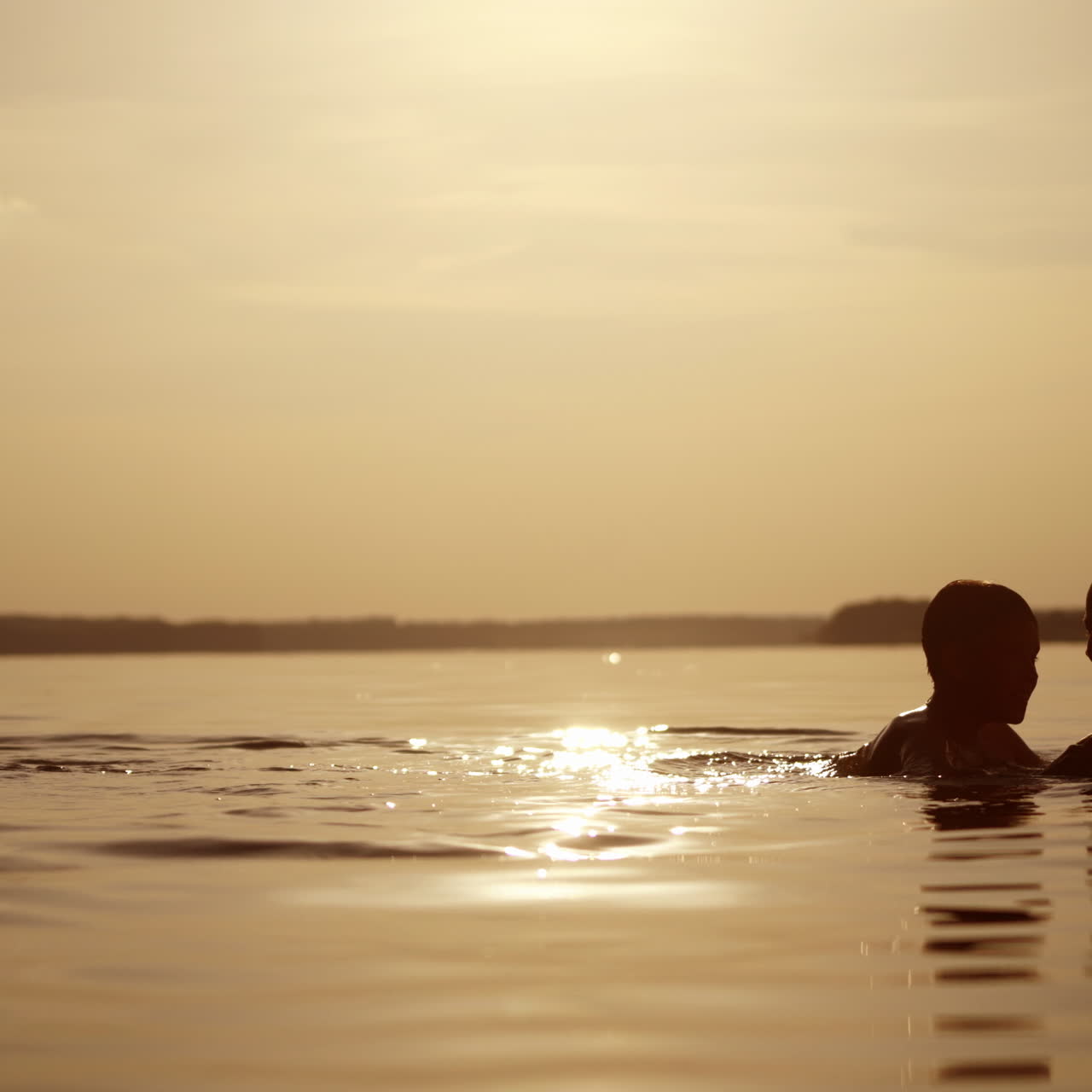 Woman and two boys in water at sunset. Mother throws her sons up into water in the evening. Children having great time with their mother in the lake at summertime.
