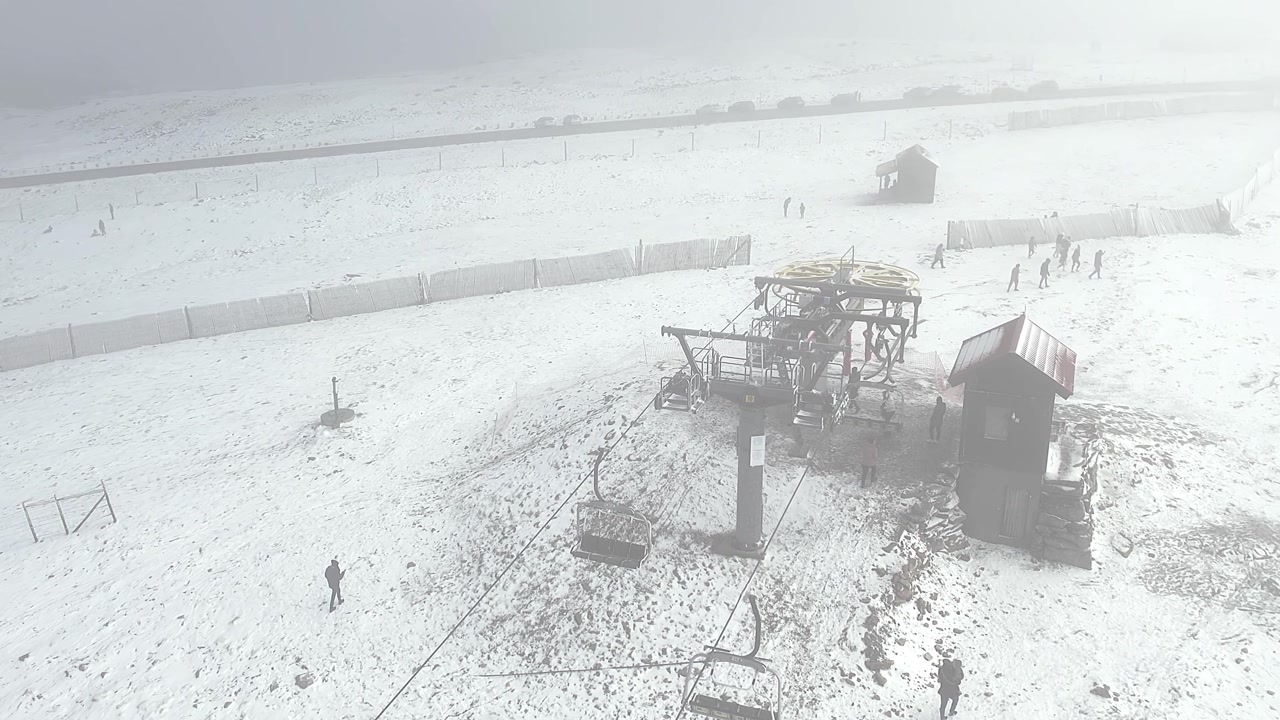 Serra da Estrela ski resort under a blizzard, displaying a damaged chairlift station and infrastructure in heavy snow, with maintenance crew inspecting the site after the storm, overhead drone shot