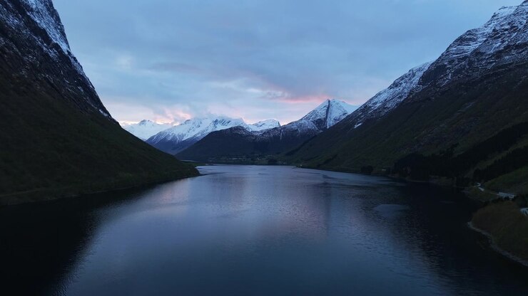 Un fiordo tranquillo riflette montagne innevate sotto un cielo crepuscolare in Norvegia. Perfetto per documentari di viaggio e natura