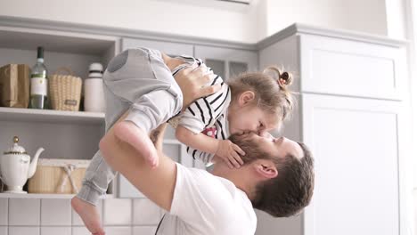 el padre sostiene a una hija pequeña en sus brazos en la cocina, la hija besa a su padre en la cocina