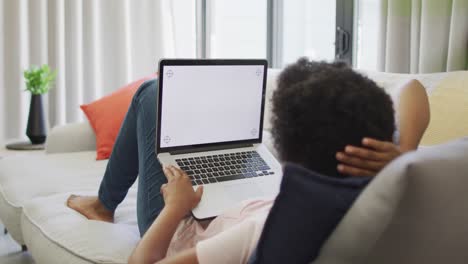 feliz mujer afroamericana sentada en el sofá, usando una computadora portátil con espacio de copia