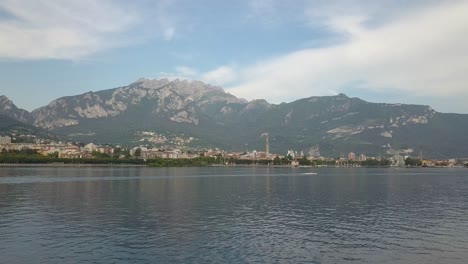 Antena-Sobre-Un-Lago-En-Italia-Hacia-Un-Pueblo-Debajo-De-Una-Montaña,-Lago-Como,-Italia