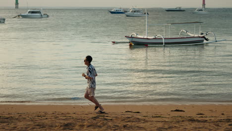 Un-Hombre-Asiático-En-Cámara-Lenta-Corre-Por-La-Playa-De-Bali-Con-Gafas-De-Sol-Al-Atardecer-En-Vacaciones-De-Cerca