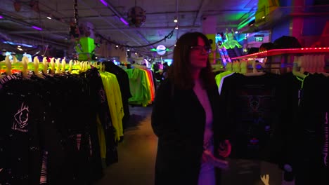 woman shopping in camden's cyberdog store, surrounded by neon clothes and futuristic decor