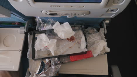 folding table for food in the cabin of the aircraft. lots of plastic and paper packaging. garbage and waste of a commercial flight