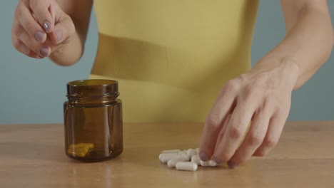 close up shot of woman's hands placing white pills into a transparent bottle