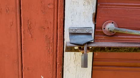 4K-60FPS-Old-Shed-Red-Door-Locked-With-Metal-Bar-and-a-Rusty-Padlock---Truck-Shot