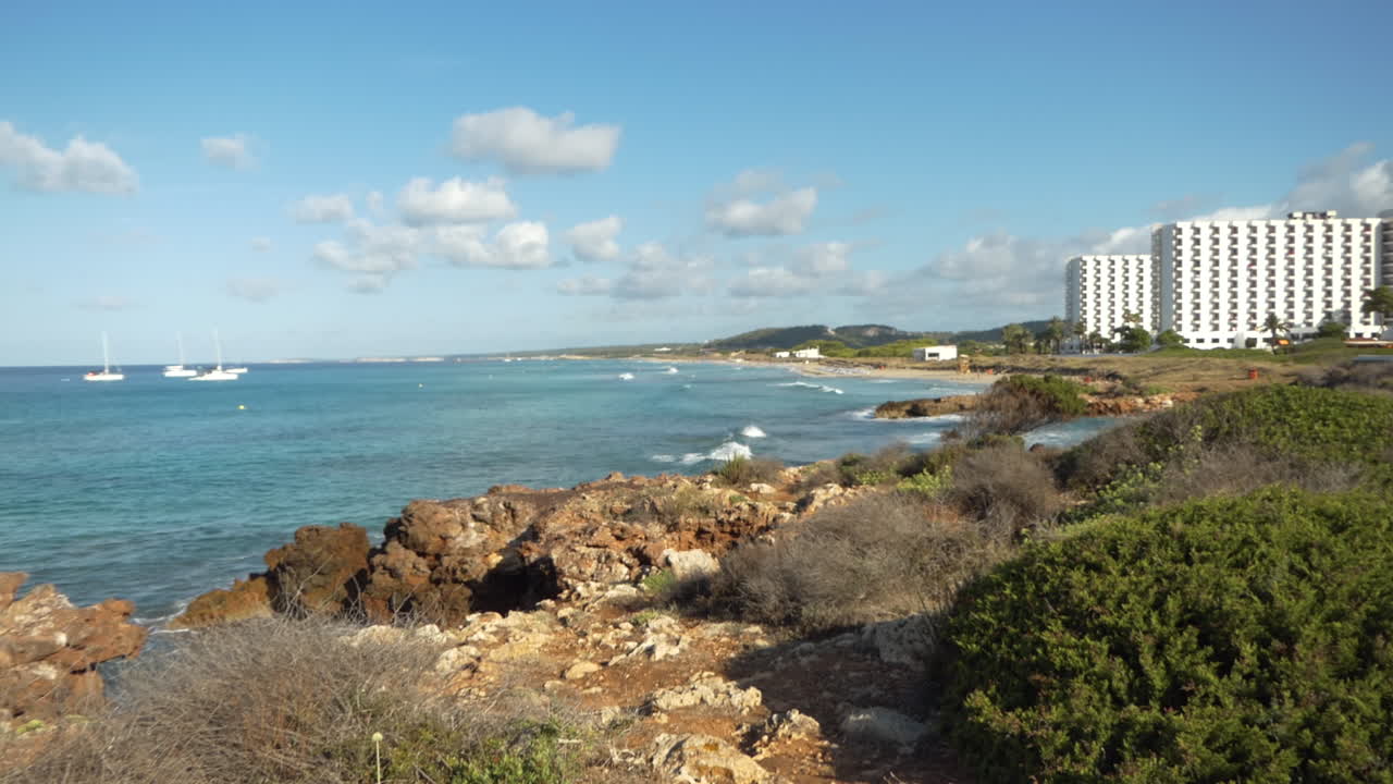 vista lateral de la playa y resort de son bou de menorca temprano en la mañana con olas regulares en el agua de mar, islas baleares, españa