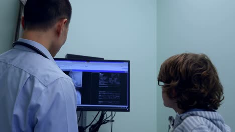 vista trasera de un joven médico asiático que le muestra a un paciente caucásico rayos x en una pantalla de computadora 4k
