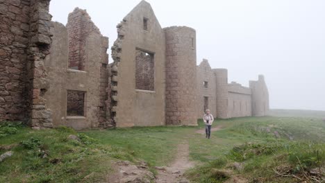 lady walker walks along the front of slains castle ruin in the mist