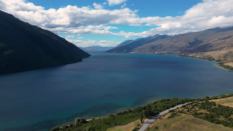 blue lake in between mountains with countryside road in new zealand, aerial view