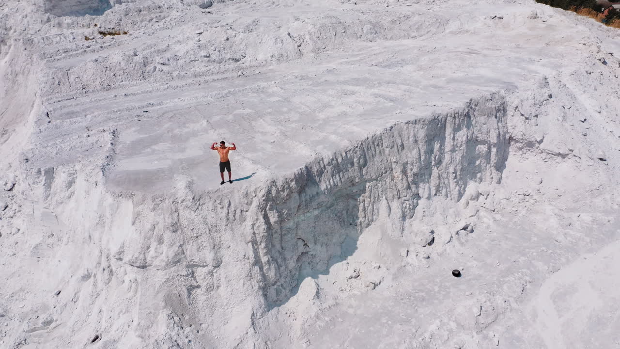 Shirtless sportsman on the rocky canyon. Aerial view of a strong man posing on the top of the hill in summer. Natural mountainous background.