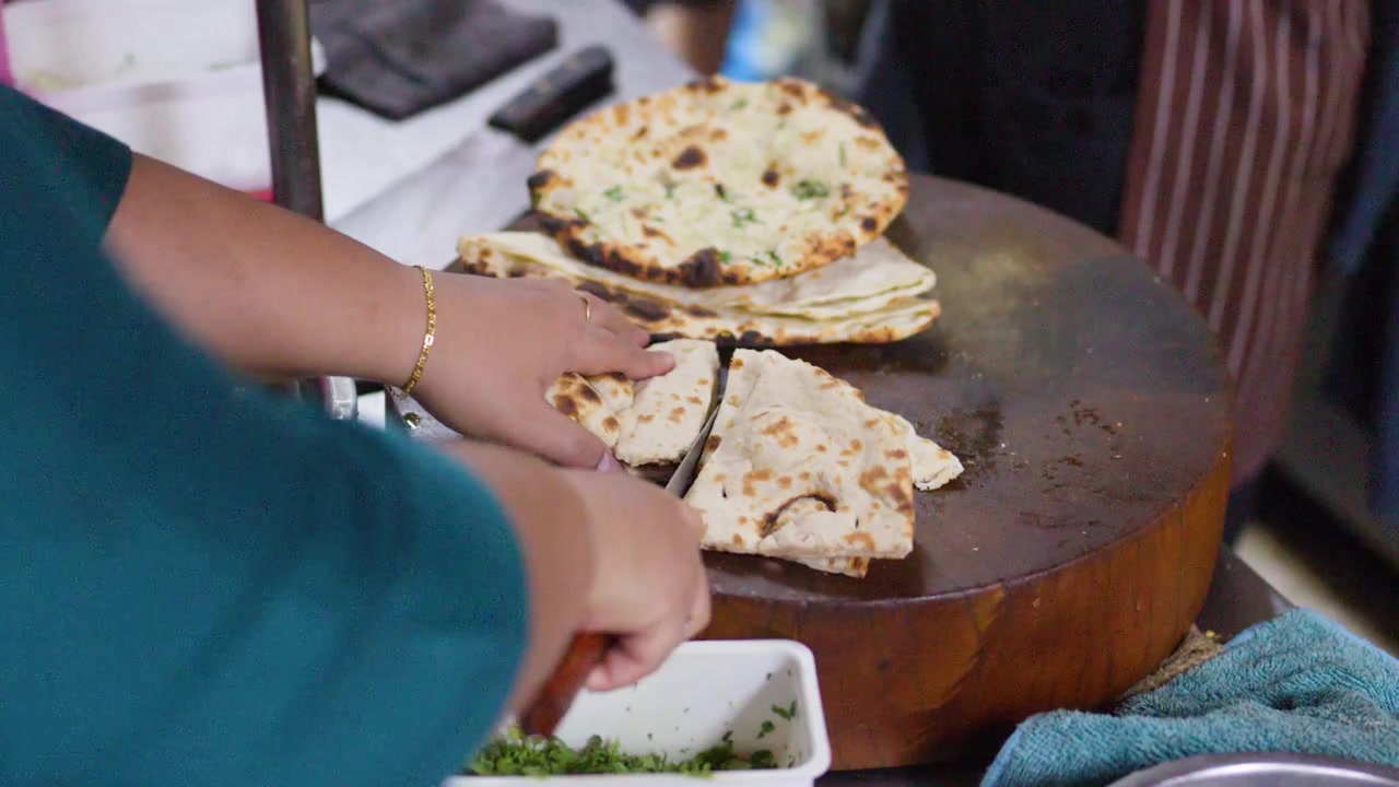 Close-up Tangan Memotong Roti Pipih di Atas Balok Kayu Bundar di Dapur Jajanan Kaki Lima