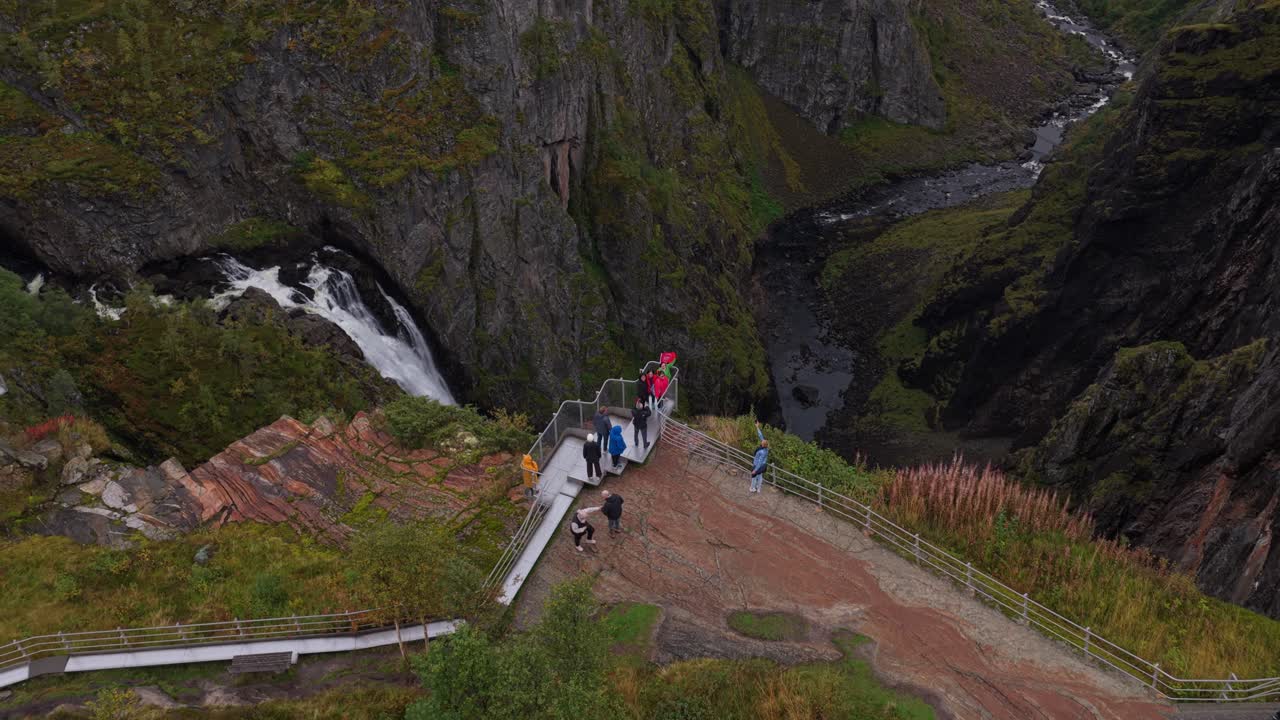 Passaggio aereo sopra Vøringfossen mentre i visitatori passeggiano lungo i sentieri a picco.
