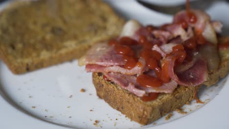 red sauce, ketchup, being poured over a bacon sandwich with brown bread